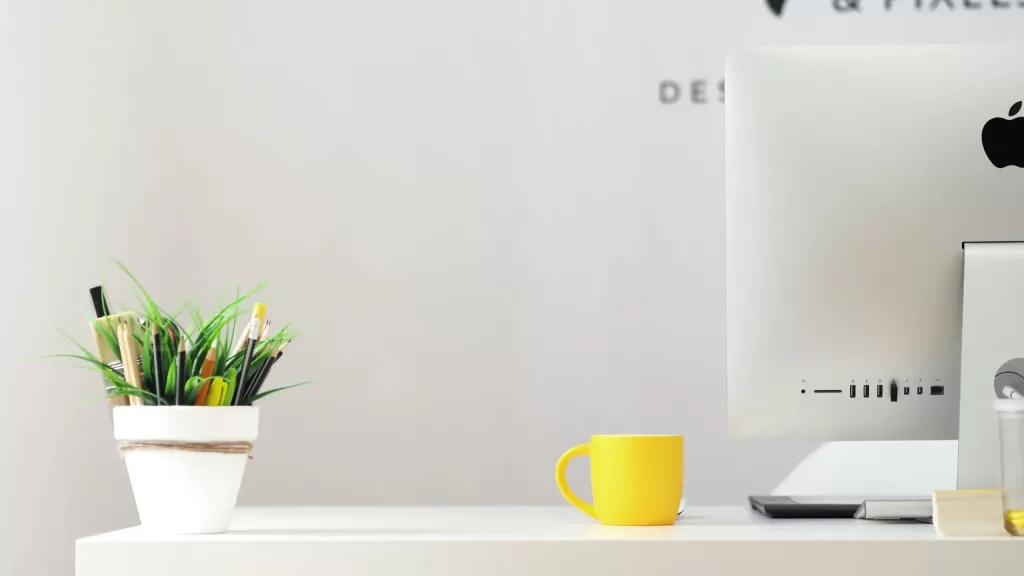 Desk with a yellow mug, a flower pot with pencils, and a desktop computer